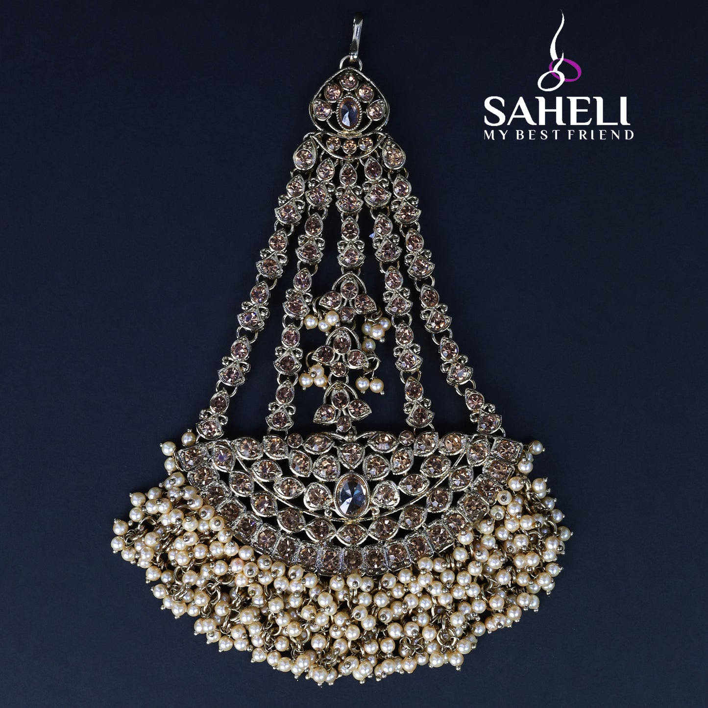 Decorative headpiece with pearls and crystals on a dark background, featuring the brand 'Saheli'.