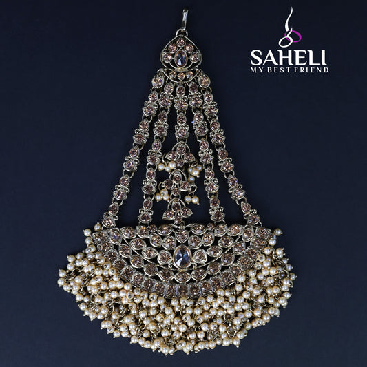 Decorative headpiece with pearls and crystals on a dark background, featuring the brand 'Saheli'.