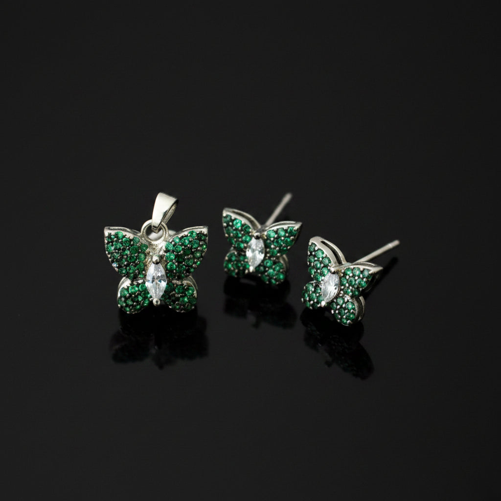 Butterfly-shaped earrings with green gemstones on a gray background, branded 'Saheli'.