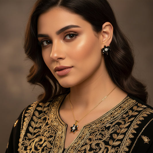 Pair of flower-shaped earrings with black and gold details on a gray background, branded 'SAHELI'.