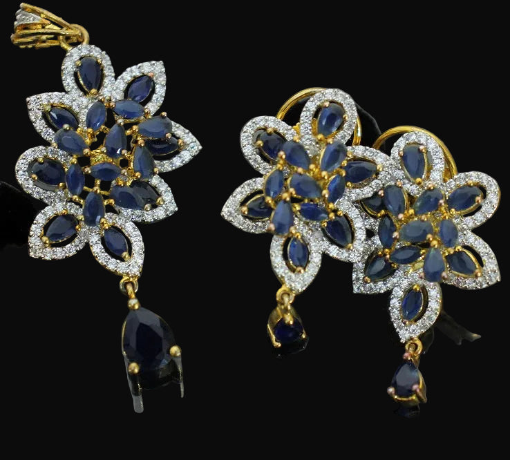 Pair of gold and blue gemstone earrings on a dark background with 'Saheli' branding.