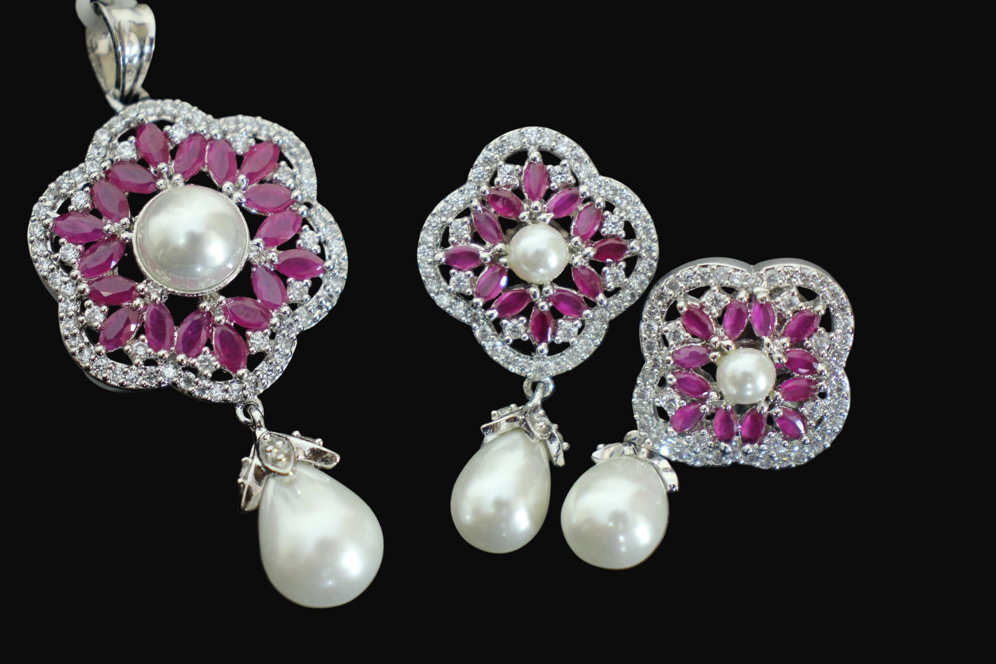 Jewelry set with pink gemstones and pearl drops on a dark background, featuring the brand 'Saheli'.