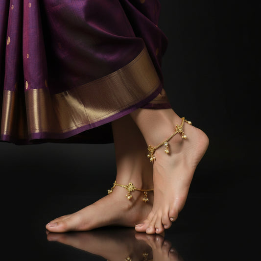 Gold anklets on a foot with a purple saree against a black background