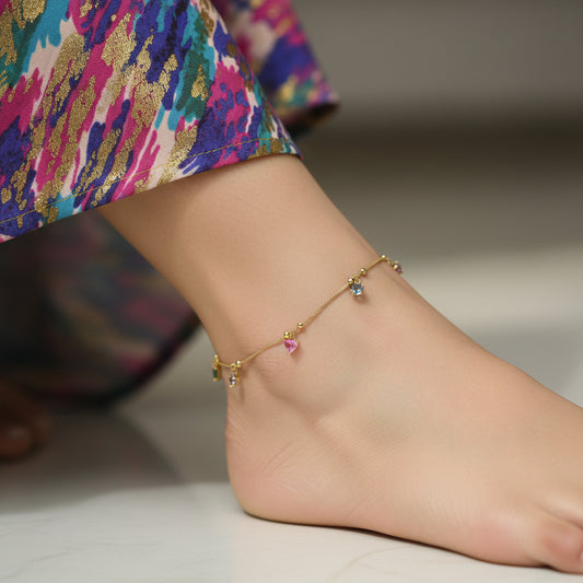 Gold bracelet with colorful charms on a dark background, featuring the brand 'Saheli'.