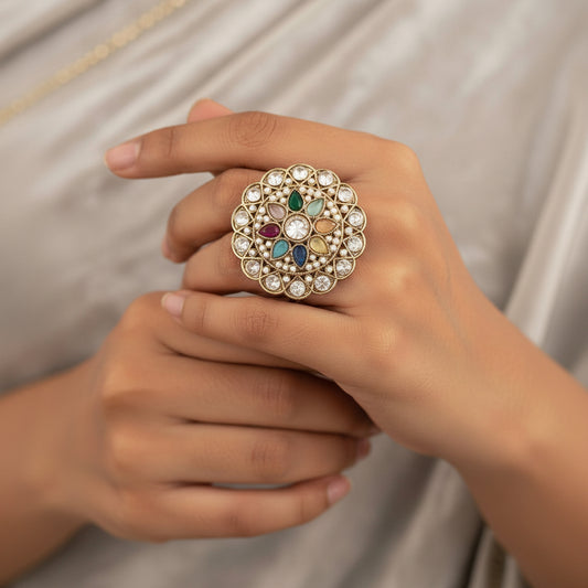 Gold-plated ring with a highly detailed, circular mandala-style filigree design, featuring clear stones and colorful enamel accents in green, blue, pink, orange, and yellow. Shown from both front and back views on a split beige and white background.