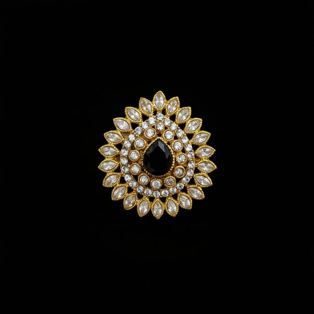 A gold-toned floral brooch featuring a central black teardrop-shaped stone surrounded by clear marquise and round crystals, displayed on a dark reflective surface with the SAHELL MY BEST FRIEND logo in the top left corner.