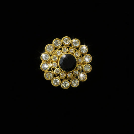 A gold-toned floral brooch featuring a prominent round black center stone surrounded by multiple clear rhinestones in a circular arrangement, displayed on a dark gray reflective surface with the SAHELL MY BEST FRIEND logo in the top-left corner.