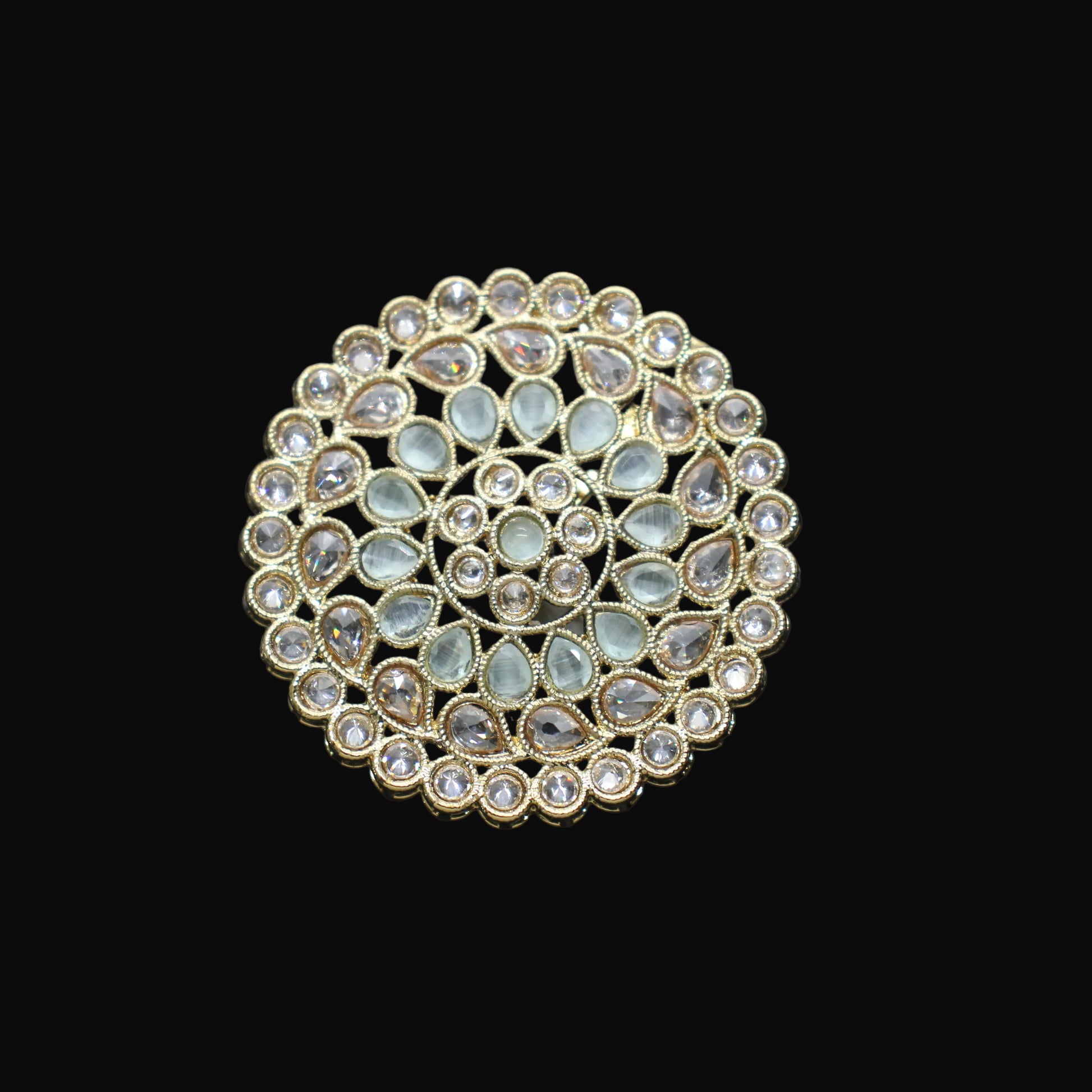 Gold and gemstone brooch on a black mannequin hand against a dark background