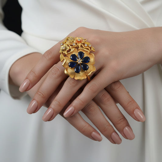 Gold and black floral ring on a black hand with 'SAHELI' branding.