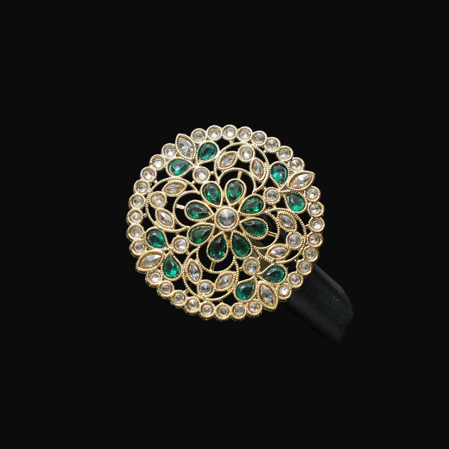 Decorative ring with green gemstones on a black mannequin hand against a dark background