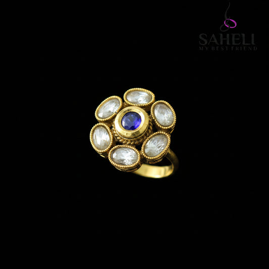 Gold ring with a blue gemstone on a gray background, branded 'Saheli'.