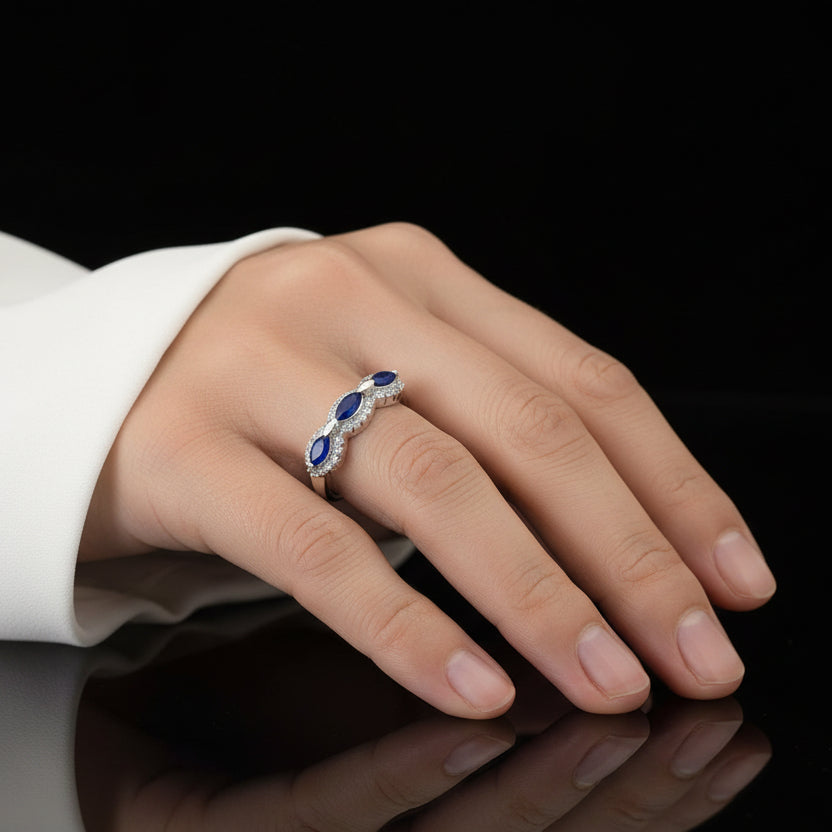 Elegant ring with blue gemstones on a black mannequin hand, branded 'Saheli'.