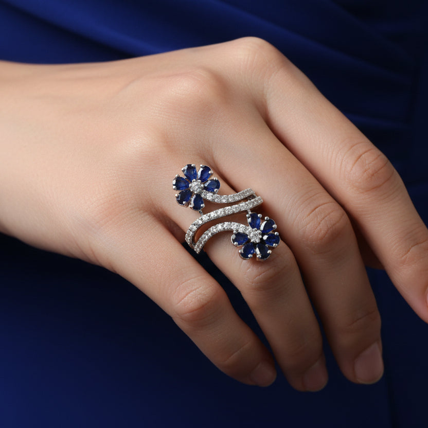 Silver ring with blue gemstones on a black-gloved hand, brand 'Saheli' visible.