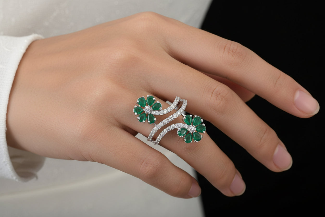 Jewelry with green gemstones and silver accents on a dark fabric background, featuring the brand 'Saheli'.