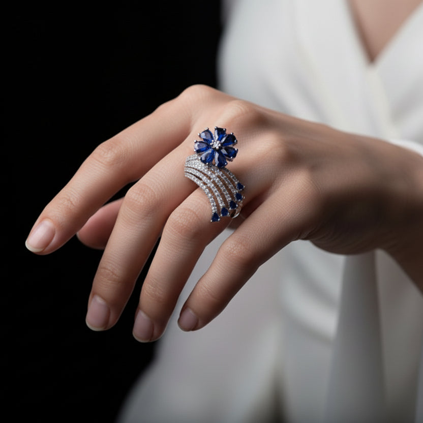 Silver ring with blue gemstones on a black mannequin hand, branded 'Saheli'.