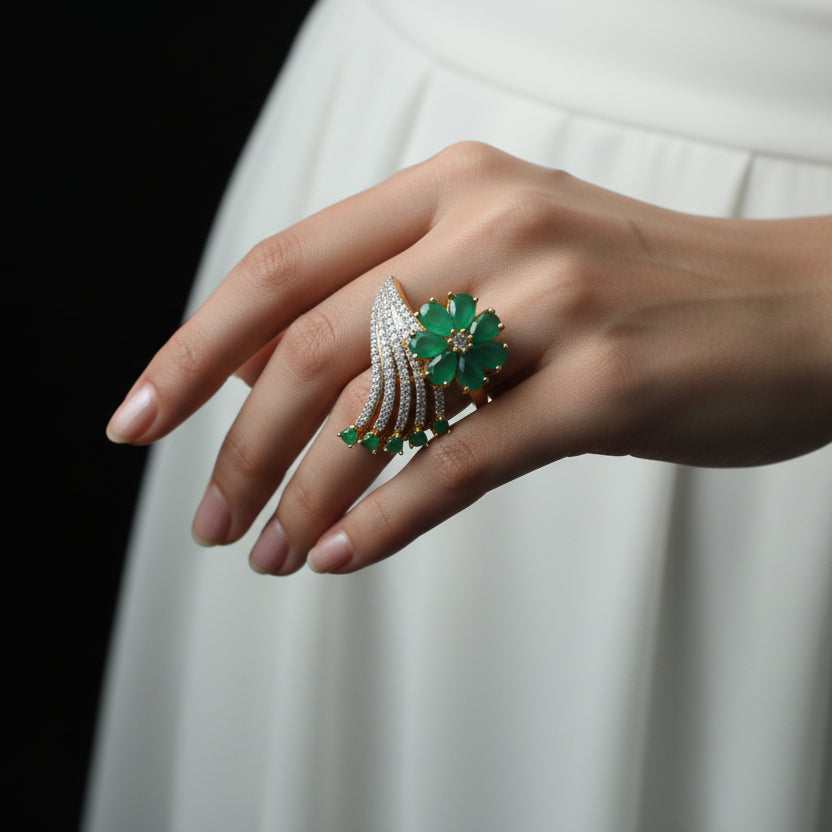 Gold ring with green gemstones on a dark background, featuring the brand 'Saheli'.