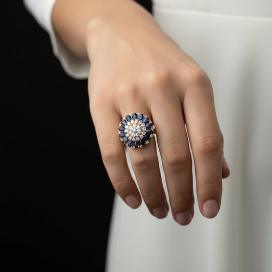 Gold ring with blue gemstones and a central diamond on a gray background, branded 'Saheli'.