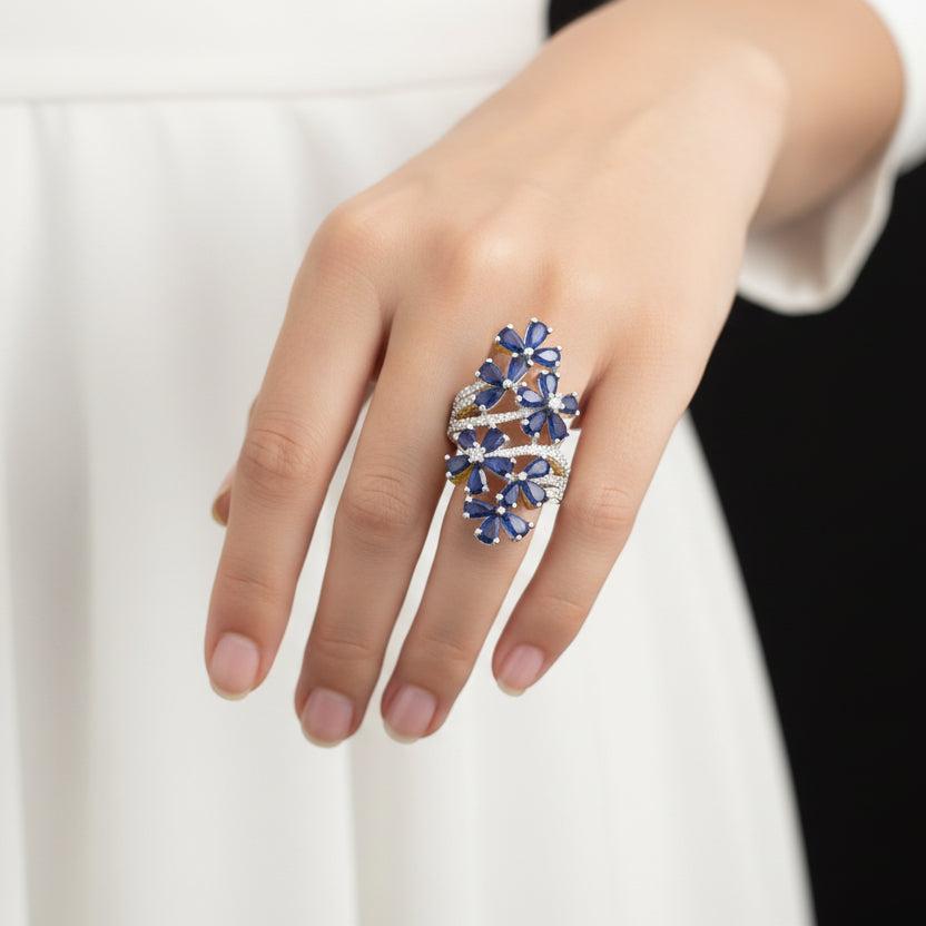 Blue gemstone ring with gold accents on a gray background, featuring the brand 'Saheli'.