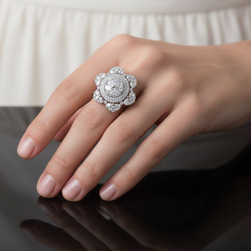 Silver ring with a large central gemstone and smaller stones on a dark background, branded 'SAHELI'.