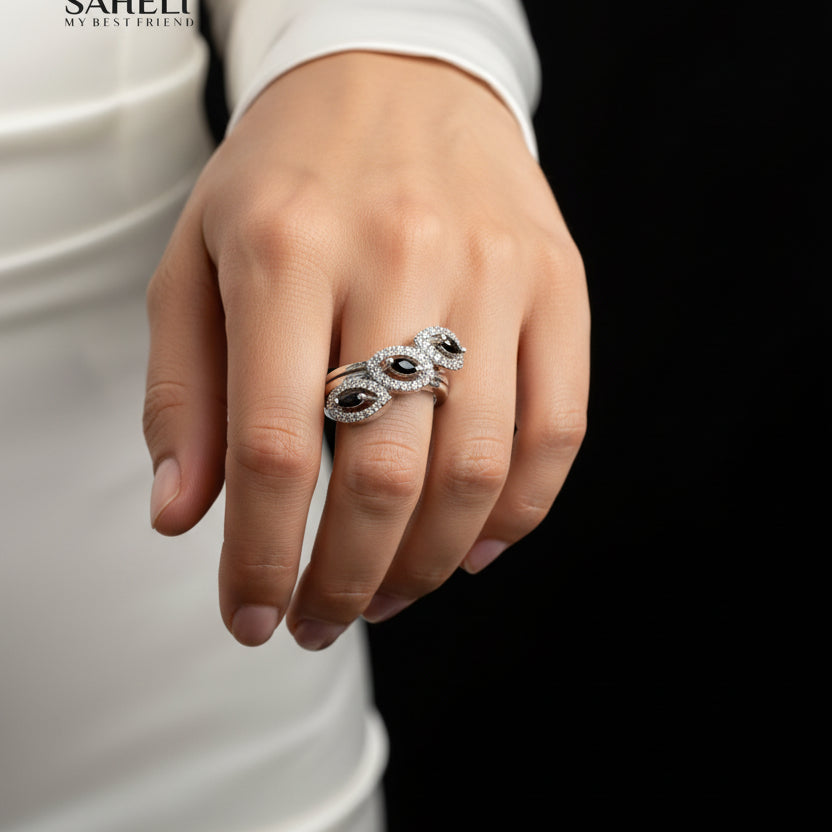 Silver ring with a clear gemstone on a gray background, branded 'Saheli'.