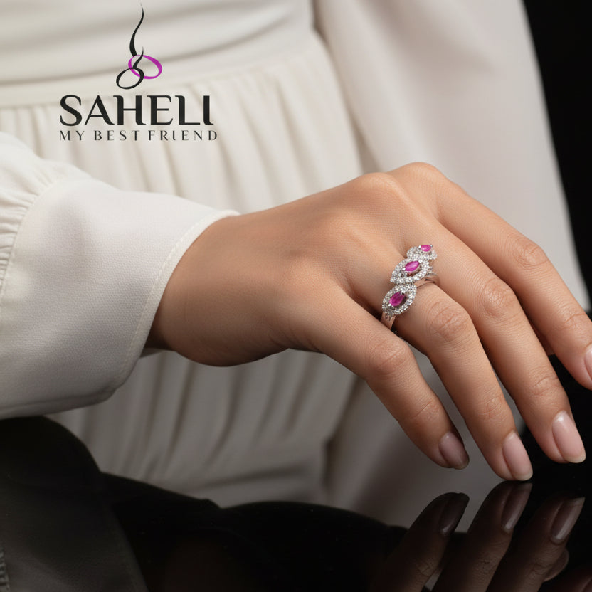 Silver ring with pink gemstones on a gray background, featuring the brand 'Saheli'.