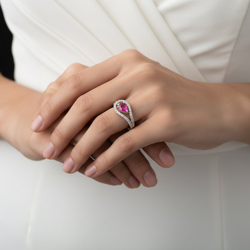 Silver ring with a pink gemstone on a black hand model, branded 'Saheli'.