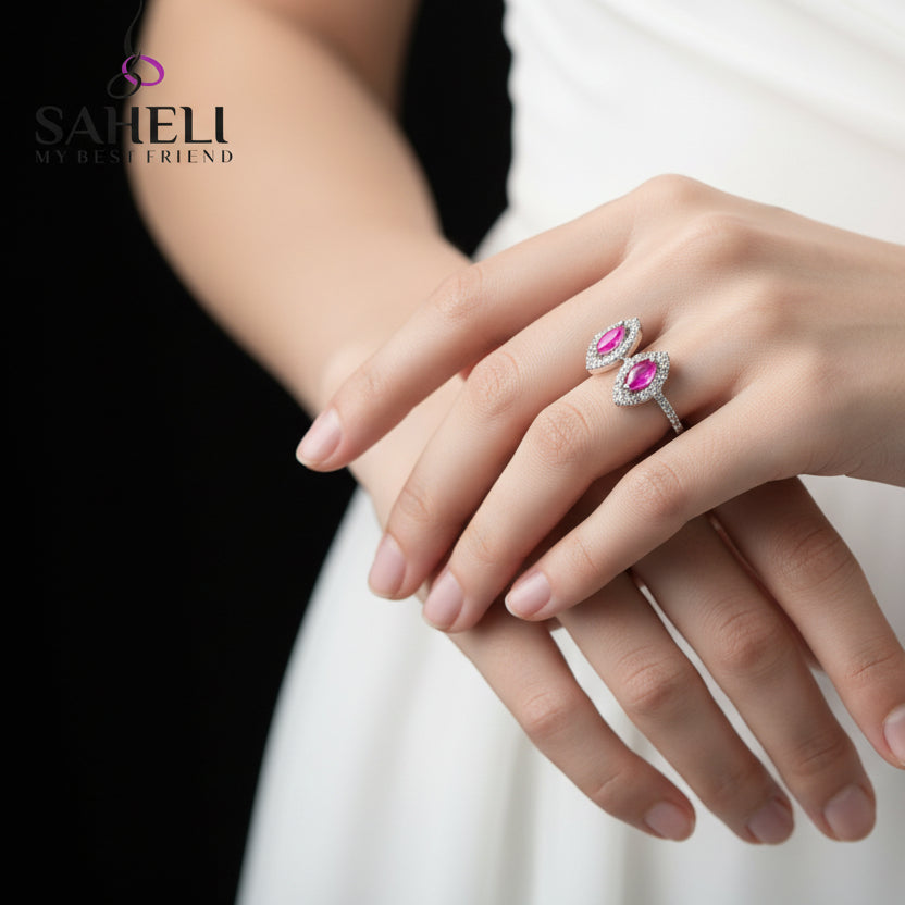 Silver ring with pink gemstones on a black glove, featuring the brand 'SAHELI'.