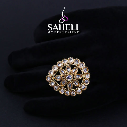 Gold and crystal brooch on a black background with 'Saheli' brand logo.