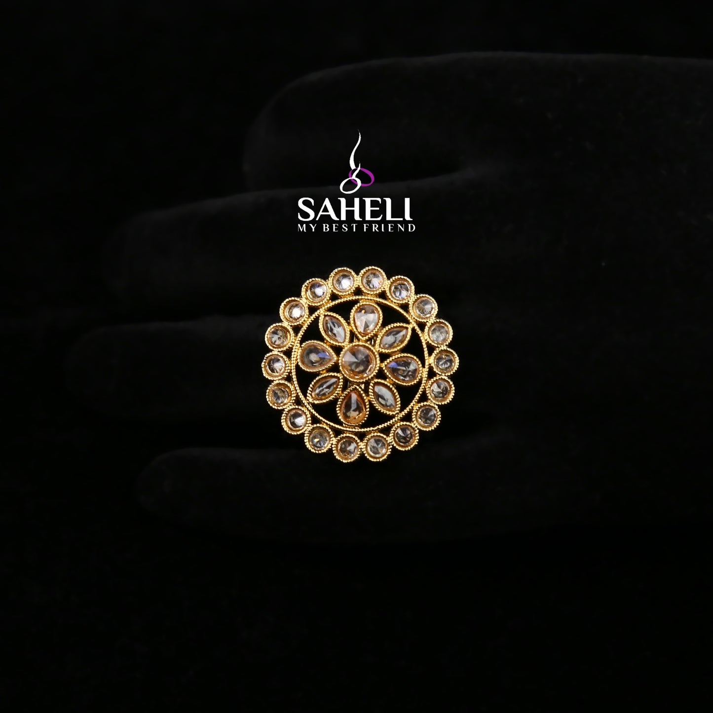 Gold brooch with gemstones on a black background, featuring the 'Saheli' brand.