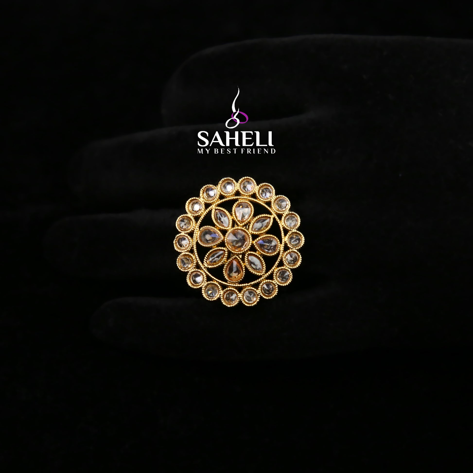Gold brooch with gemstones on a black background, featuring the 'Saheli' brand.