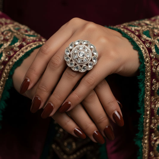 A large ornate silver-toned ring with clear stones is displayed on a black velvet glove hand against a black background. The brand name 'SAHeli' is visible as an overlay near the top center.