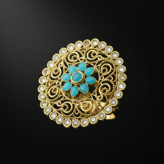 An ornate circular gold filigree brooch featuring a central turquoise flower motif and a border of small white stones, displayed on a dark gray background with a 'SAHELL MY BEST FRIEND' watermark in the top right.