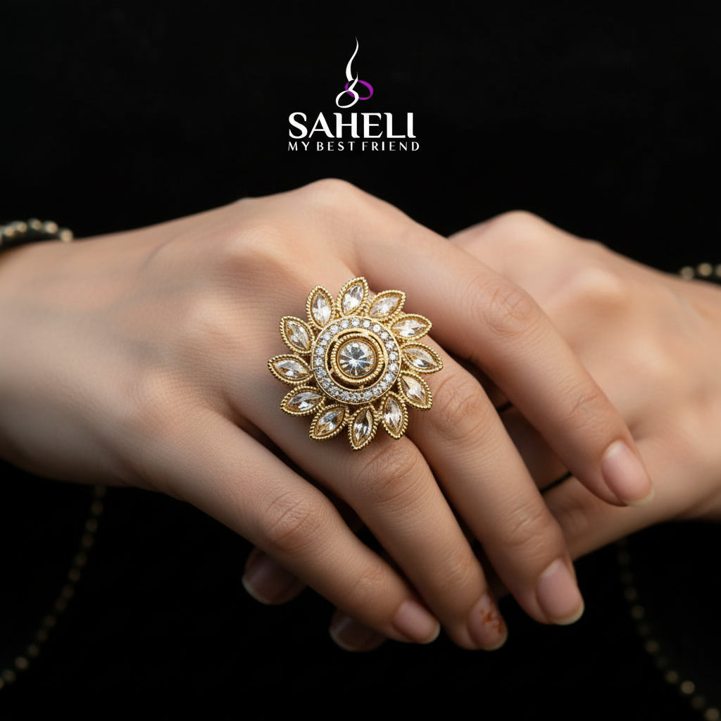 A gold-toned ornate ring with a floral mandala design and clear stones, displayed on a black velvet glove hand against a black background. The brand name 'SAHELI MY BEST FRIEND' is printed in white text over the center.
