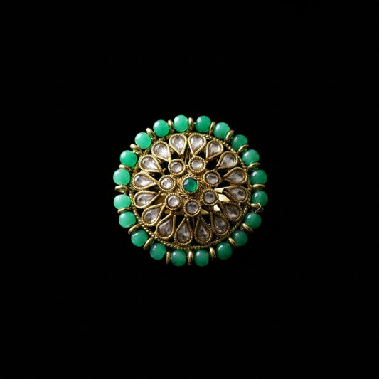 A gold-plated Indian Kundan ring with green stones and clear inlay stones, displayed on a black mannequin hand against a dark gray background. The brand logo 'SAHELL MY BEST FRIEND' is visible in the top left corner.