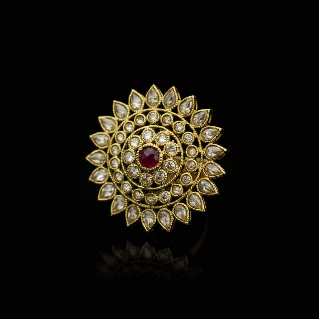 A gold-toned Indian style Kundan choker brooch featuring a central red ruby stone surrounded by clear stones in a sunburst pattern, displayed on a dark gray reflective surface.