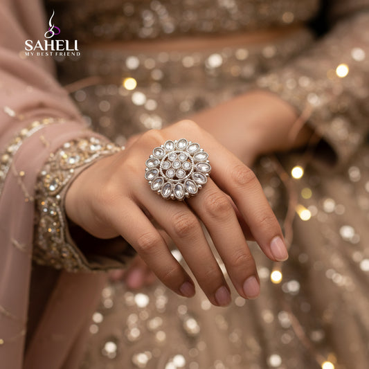 A large, ornate silver-toned ring with clear stones is displayed on a black velvet glove hand against a black background. The brand logo 'SAHELI MY BEST FRIEIND' is visible near the top center.