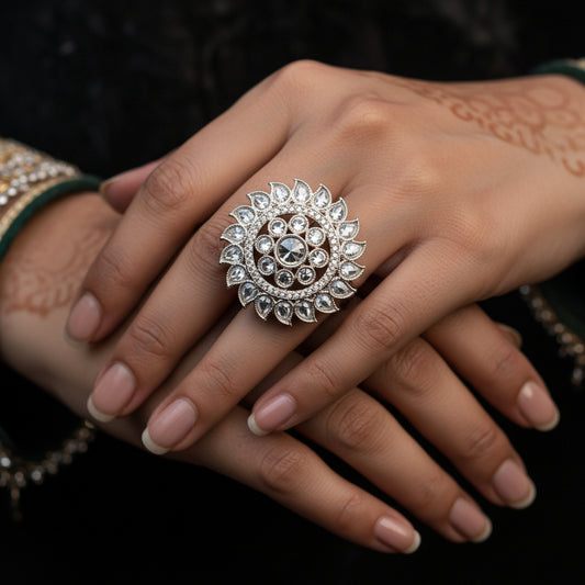 A large, ornate silver-toned statement ring with a central clear gemstone and surrounding intricate crystal or diamond-like detailing, displayed on a black velvet glove hand. The brand logo 'SAHELI MY BEST FRIEND' is visible in the upper center.