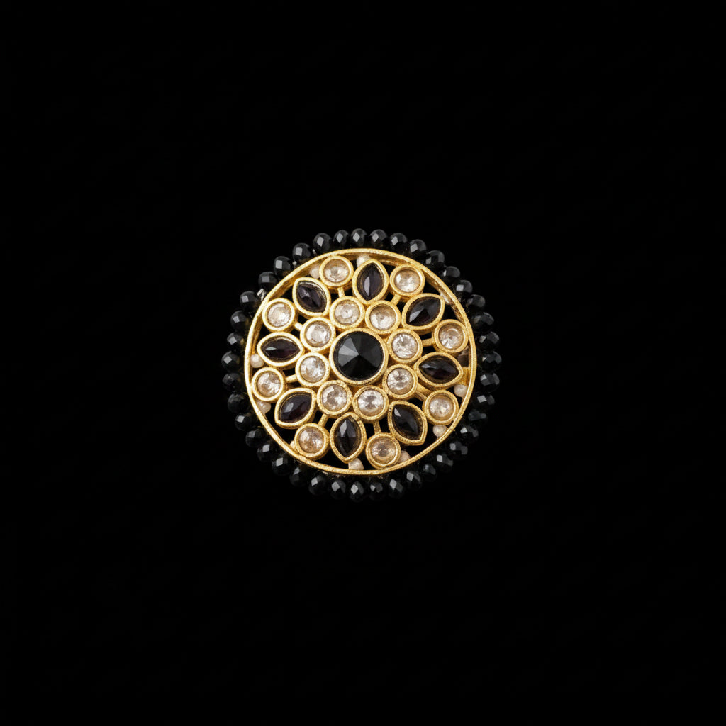 A round gold-toned statement ring with black stones and clear stones, displayed on a reflective gray surface with the 'SAHELI MY BEST FRIEND' logo in the top left corner.