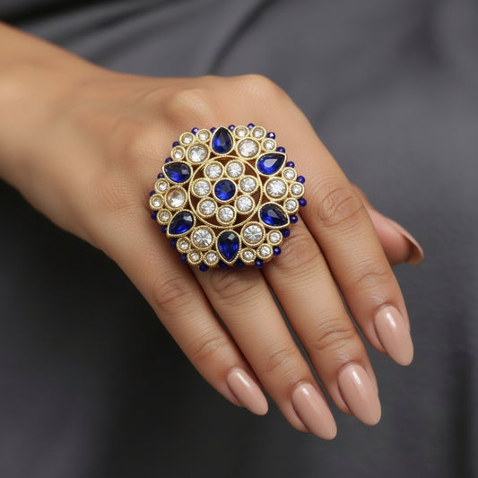 A gold-toned decorative brooch or pin featuring blue teardrop-shaped stones and small clear rhinestones, displayed on a black background next to a white price tag.