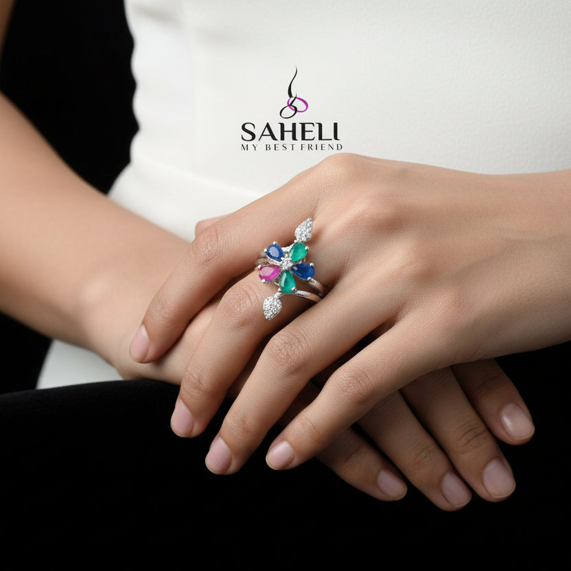 Silver ring with colorful gemstones on a gray background, featuring the brand 'Saheli'.