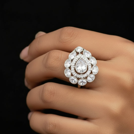 A silver-toned teardrop-shaped ring with clear stones and intricate detailing, displayed on a black velvet gloved hand against a dark background. The brand logo 'SAHELI MY BEST FRIEND' is visible in the center.
