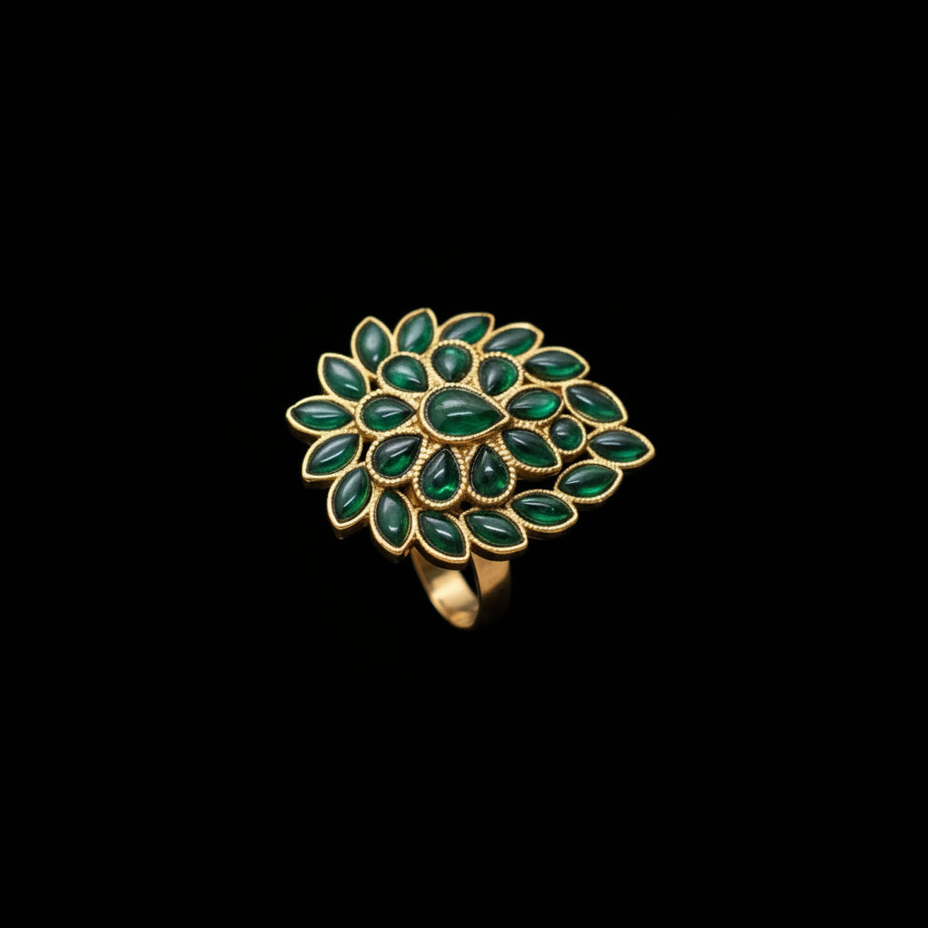 A gold ring featuring a large, flower-like cluster of green stones, displayed on a black mannequin hand. The brand logo 'SAHELI JEWELLERY' is visible in the top right corner.