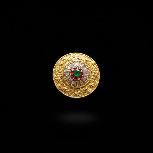 A large gold-toned statement ring displayed on a black mannequin hand. The ring features an intricate circular design with a central red and green motif surrounded by clear stones, set against a dark gray background with a 'SAHELL' watermark in the top left corner.