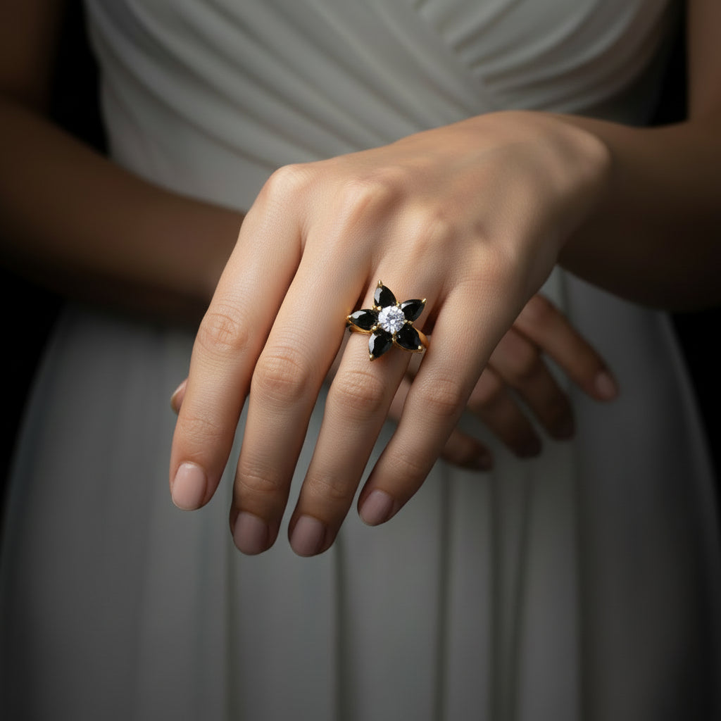 Gold ring with black gemstones and a diamond on a gray background, featuring the brand 'SAHELI'.