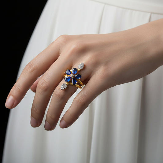 Gold and blue gemstone ring on a black mannequin hand with 'SAHELI' branding.