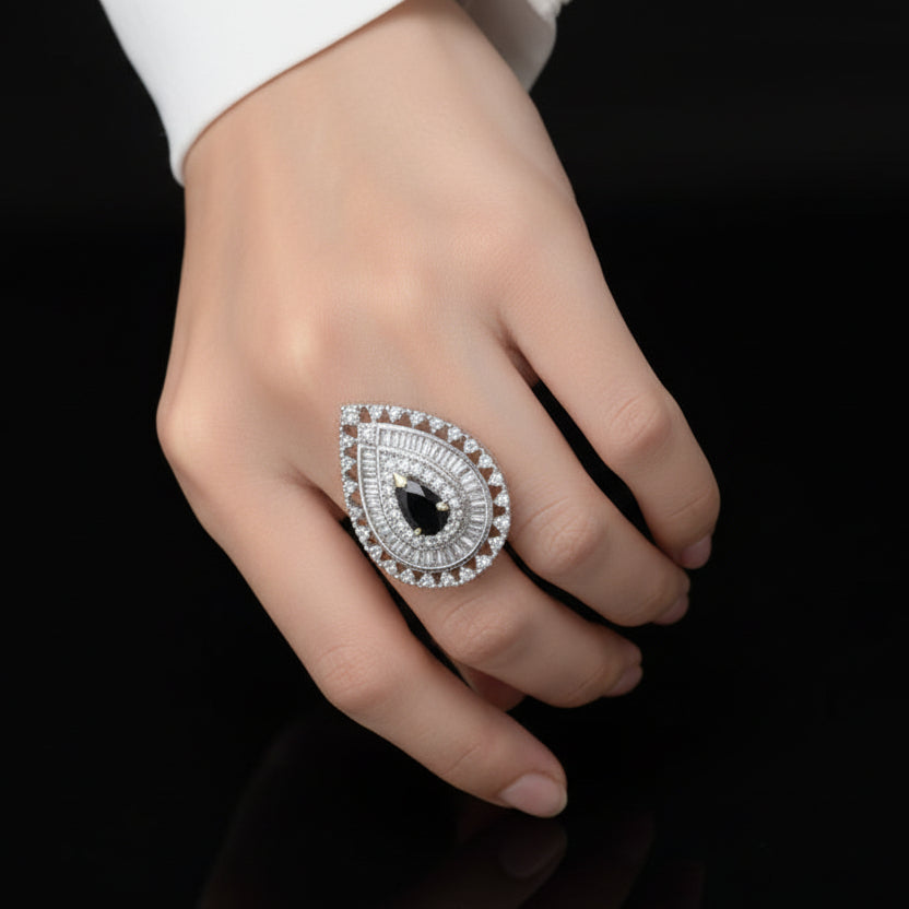 Teardrop-shaped diamond earring with black gemstone on a reflective surface, branded 'Saheli'.