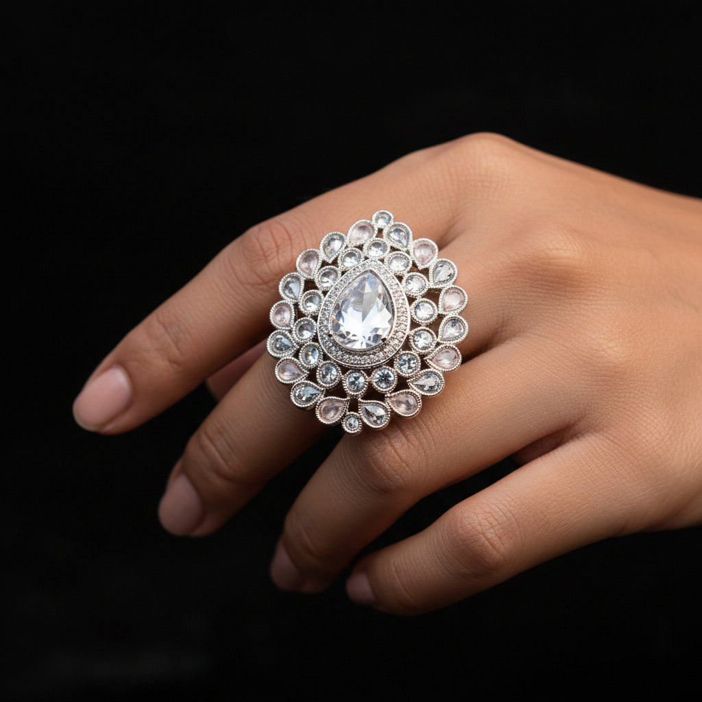 A large ornate silver-toned statement ring with a teardrop-shaped clear crystal and surrounding clear stones, displayed on a black gloved hand against a black background. The brand name 'SAHeli My Best Friend' is visible as an overlay.