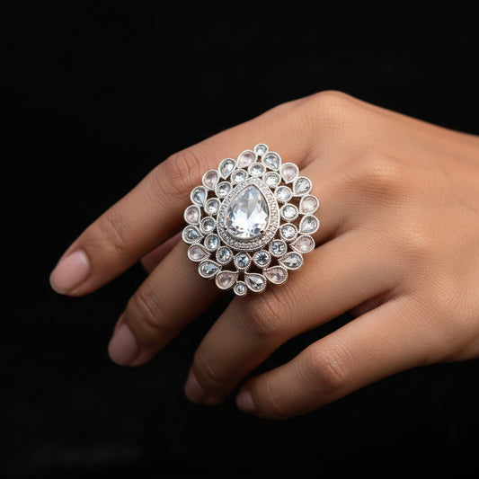 A large ornate silver-toned statement ring with a teardrop-shaped clear crystal and surrounding clear stones, displayed on a black gloved hand against a black background. The brand name 'SAHeli My Best Friend' is visible as an overlay.