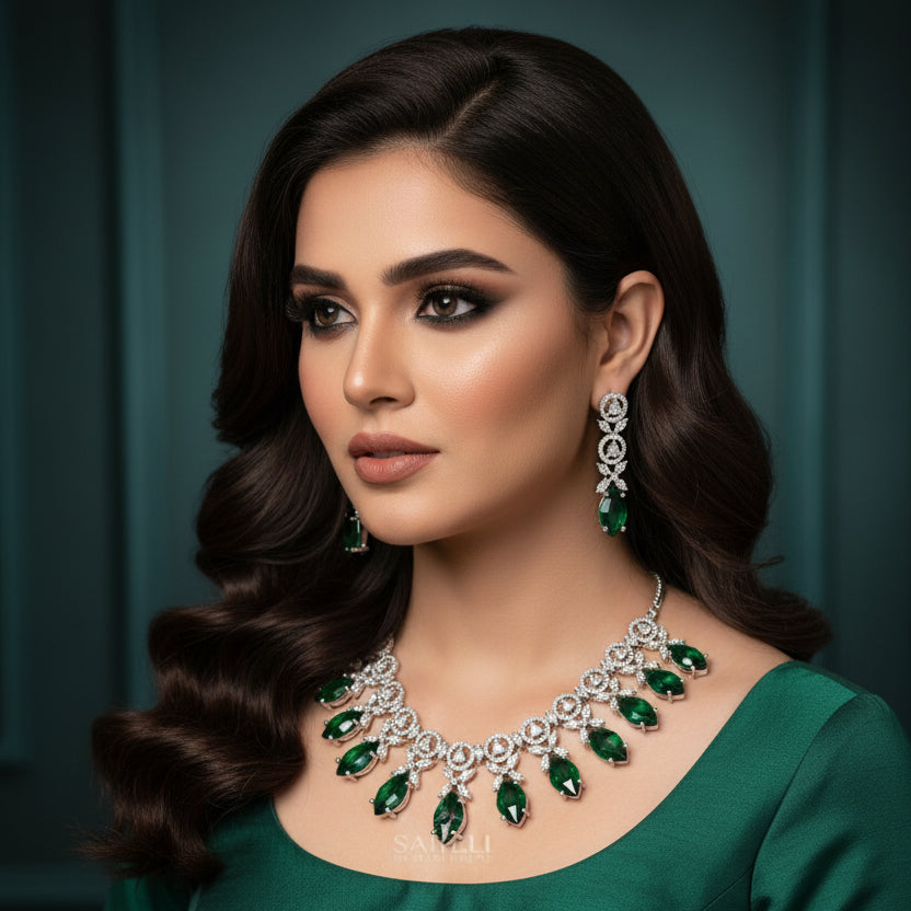 Jewelry set with necklace and earrings featuring green gemstones on a gray background, branded 'Saheli'.