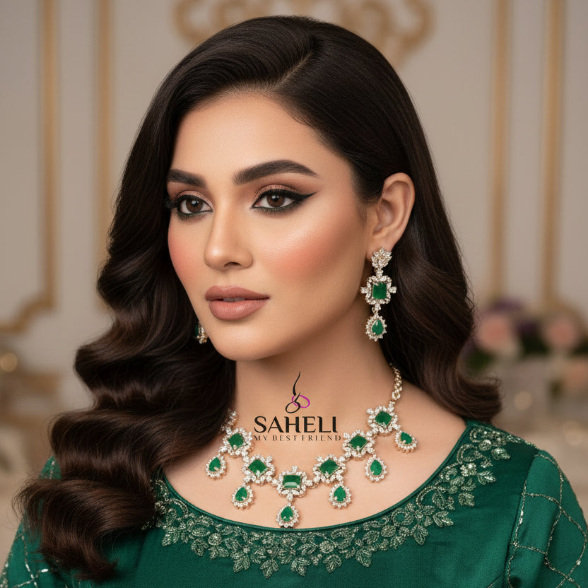 Jewelry set with emerald green stones and gold accents on a gray background, featuring the brand 'Saheli'.